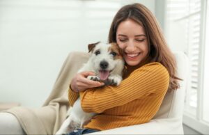 Woman smiling and holding a small white-and-brown dog while sitting indoors.